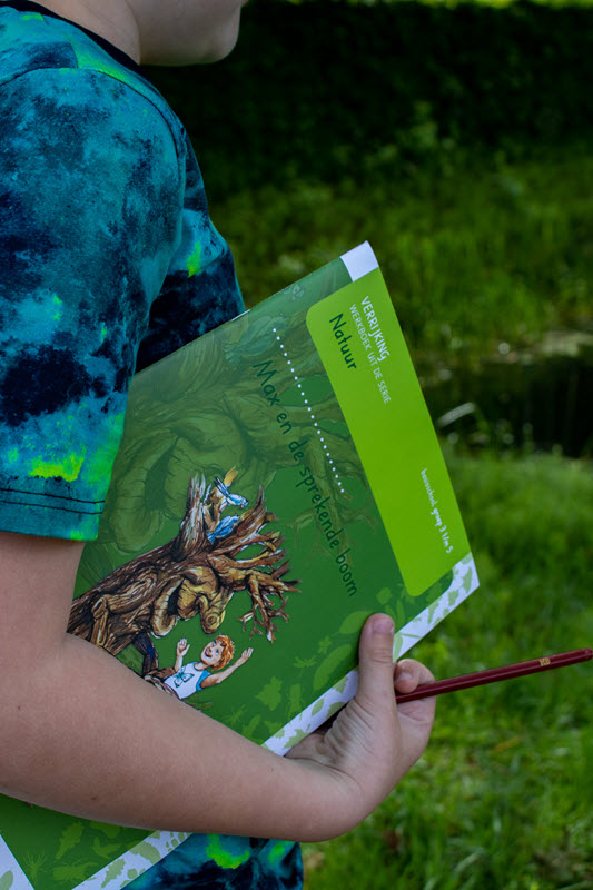 Lesmateriaal Basisonderwijs | Leerling met werkboek Max en de sprekende boom onder zijn arm. Op het werkboek Natuur staat de hoofdfiguur Max en een boom met een gezicht.