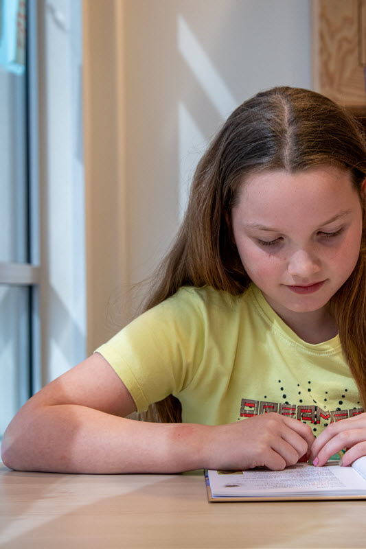 Moeite met begrijpend lezen | Meisje leest aan tafel aandachtig in een boek